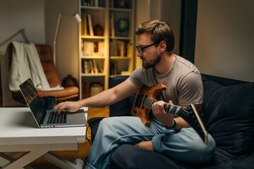 Side view of a Caucasian man sitting at home and practicing the guitar.