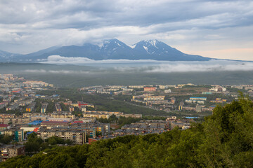 Obraz premium Beautiful landscape. Top view of residential urban areas. Volcanoes in the distance. Overcast weather. Low clouds. Summer cityscape. Petropavlovsk-Kamchatsky city, Kamchatka Krai, Far East of Russia.