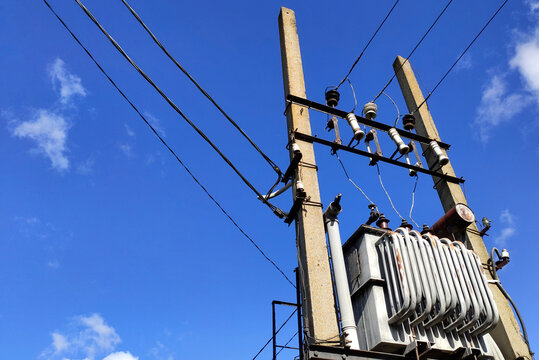Powerful electrical transformer installed outside between two poles, blue sky with clouds in the background