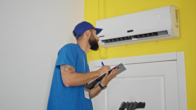 Young hispanic man technician repairing air condition machine writing report at home