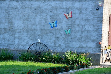 A view of a wall of an old abandoned shack, shelter, or house decorated with plastic butterflies, cart wheel and other items seen on a sunny summer day on a Polish countryside