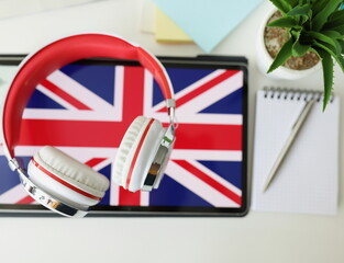 Tablet with image of British flag with headphones and notebook with pen lie on table. Learn British English remotely via app concept