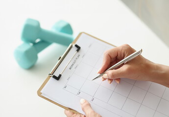 Woman makes workout plan for week next to dumbbells. Daily sports and healthy lifestyle concept