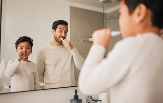 Dad, boy and child brushing teeth in mirror for hygiene, morning routine and teaching healthy oral habits at home. Father, kid and dental cleaning in bathroom with toothbrush, fresh breath and care - Powered by Adobe
