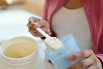 Young athletic woman pouring protein powder into a cup, drinking supplement for muscle after workout at home