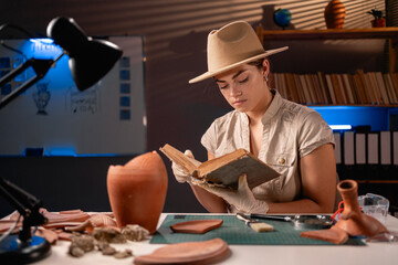 Archeologist working late night in office reading old book about archaeology