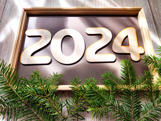 Wooden figures and numbers of the new year 2024 with frame and fir branches of Christmas tree....