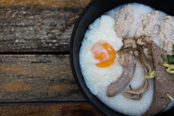 Congee with minced pork, entrails and boiled egg in bowl in black bowl on a wood background.