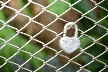 Heart shape keychain and wire metal fence net on the blurry forest background,two keychains are hanging.