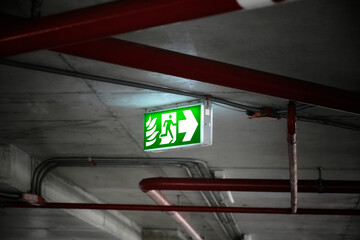 Fire exit sign or emergency singn, light in the dark on the parking lot in the building, exit singn in the dark light, close-up sing. - obrazy, fototapety, plakaty