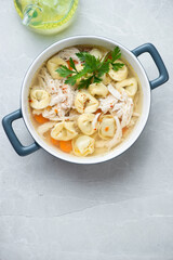 Bowl of tortellini and chicken soup on a light-grey granite background, vertical shot with space, top view