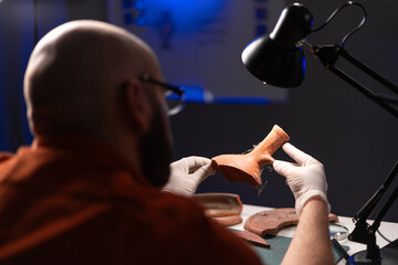 Bald archaeologist working at night in the office studying ancient artifacts
