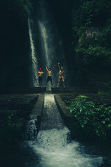 Obraz premium A man standing on a rock in front of a tall waterfall in the mountains, set in the tropical landscape of Jibhi Waterfall, Himachal Pradesh, India.