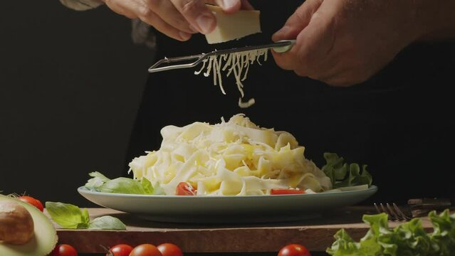 Chef grating cheese onto freshly prepared dish with boiled noodles, traditional Italian Mediterranean food. Great background for your projects. 