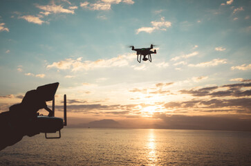 Silhouette of remote control a flying drone which taking photo over sunrise sea