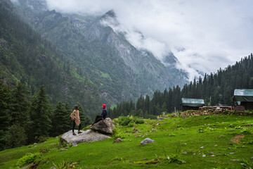 Young male hiker's with backpack relaxing on top of a mountain during Cloudy Weather - scenery from vacation - photo with space for your montage, Himachal Pradesh, Jibhi kheerganga, India.