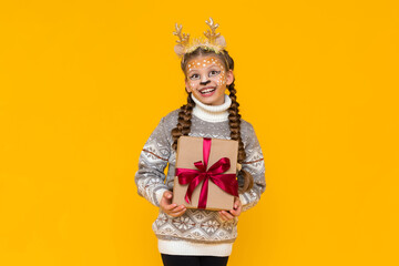 A child dressed as a Christmas reindeer is holding a gift box with a beautiful red bow. New Year's...