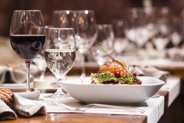 Elegant Dining Experience: A Cozy Restaurant Table Setting with a Delectable Salmon Salad and a Glass of Fine Red Wine, Capturing the Warm and Inviting Atmosphere