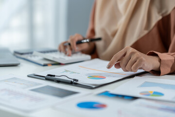 Motivated muslim businesswoman wearing hijab working on real estate project analyzing document data graph discussing presentation work income calculation tax to company in office.