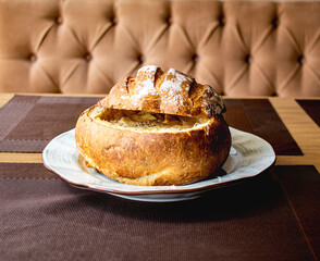 Ruddy bread, cut off top of light brown color, filled with cheese soup and served on a plate. Cheese soup baked in a bread roll.