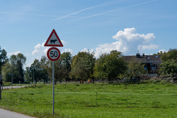 road sign Tempolimit 50 and cow warning sign red with a small farm and cows in the background