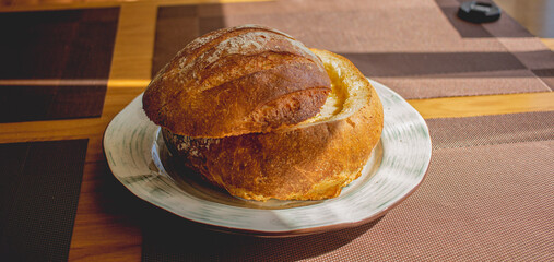 Delicious lunch. Ruddy bread, cut off top of light brown color, filled with cheese soup and served on a plate. Cheese soup baked in a bread roll.