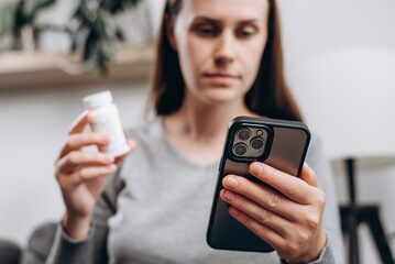 Selective focus of young lady using smartphone for reading, searching prescription on bottle medicine, pill label text about information online, instructions side effects, pharmacy medicament concept - obrazy, fototapety, plakaty