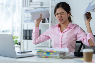Obraz na płótnie Canvas Asian female office worker stressed while working with stacks of documents and laptop. Feeling tired, headaches, and burned out at work feel sick Not happy in the office.