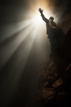 a man reaching up to god for help. standing on a steep cliff hole. bright light rays shining down. 