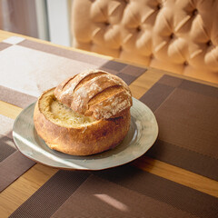 Delicious cheese soup baked in a bread roll. The golden brown bread is covered with a light brown cut top and the inside of the loaf is filled with cheese soup.