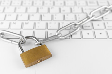 ノートパソコンのキーボードと鎖と南京錠。セキュリティのイメージ