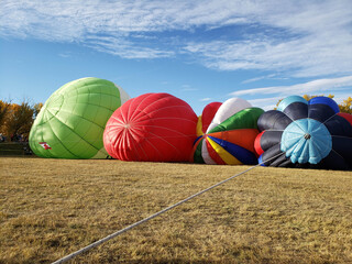Several colorful and vibrant hot air balloons lying on the ground while being inflated.
