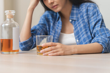 Alcoholism drunk asian young woman hand holding glass of alcohol or whiskey, female sitting alone, drinking on table at home, at night. Treatment of alcohol addiction, suffer abuse problem alcoholism - obrazy, fototapety, plakaty