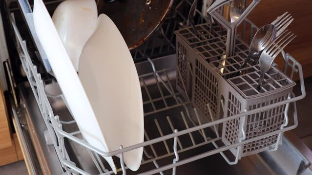 The girl loads dirty white plates into the dishwasher, using a modern appliance to maintain a clean kitchen. Housewife puts dirty dishes