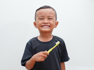 little asian boy holding a toothbrush while smiling on white background with copy space. children's dental health concept