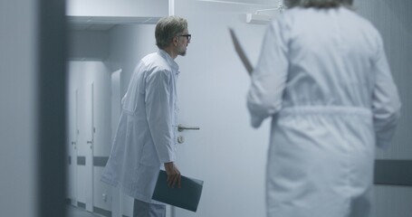 Naklejka premium Doctors take elderly woman out of the operating or procedures room on wheelchair. Senior man walks the corridor to his hospital room. Medical staff and patients in clinic or medical center hallway.
