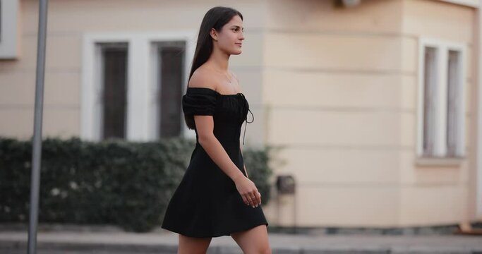 Elegant lady in black dress walking at city street, slow motion