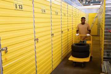 Man in work gloves is carrying cargo cart with car tires