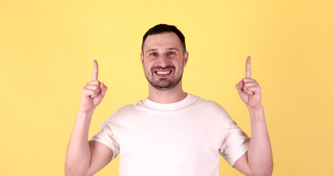 Young man in basic look camera pointing fingers hands up overhead on copy space workspace area isolated on yellow background studio. People lifestyle concept.