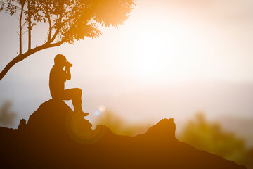 A tourist man sitting on the rock and take photo sunset orange color background - 648567823