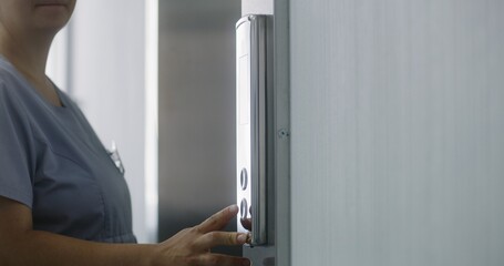 Close up shot of nurse in uniform coming to lift door, pressing call button. Healthcare specialist at work in modern clinic. Medical worker and elderly patient wait elevator in hallway.