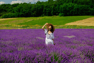 Beautiful lady in a lavender flower field on a summer day. A beautiful woman enjoys a blooming lavender field. Portrait of a young woman in a hat with a bouquet of lavender. 4K, UHD