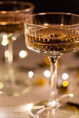 party, celebration and holidays concept - close up of champagne in glasses, electric garland lights and golden confetti on table over black background