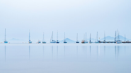 Sailing boats, reflected in the very calm, Mediterranian sea, in the Mar Menor, near Murcia Spain.  It is morning and the colours are muted. Room for Copy