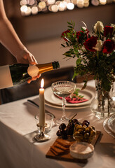 holidays, dinner party and celebration concept - close up of hand pouring champagne from bottle to glass on table at home or restaurant