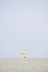 Décor minimaliste avec la plage et un parasol jaune par un jour de ciel bleu - obrazy, fototapety, plakaty