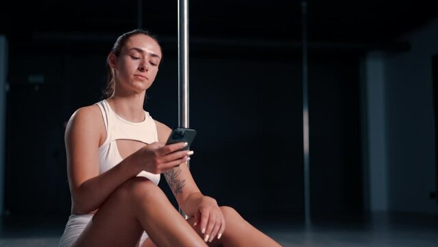 portrait of a young beautiful sexy girl after a dance class on a pole holding a phone in her hands texting with someone