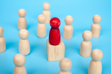 Red figure on top of wooden cube surrounded with other wooden figure.