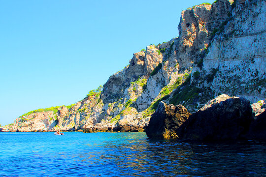 Crystalline scenery from Tremiti Islands (Isole Tremiti) with huge ridges of solid white rock in the background, interspersed with vivid green vegetation, a dinghy and big stones on the Adriatic Sea