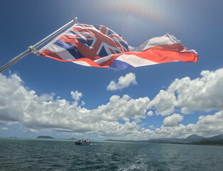 Hawaiian Flag Waving in the Blue Sky Against the Sun. Boat Trip to Kaneohe Sandbar, Oahu Island,...